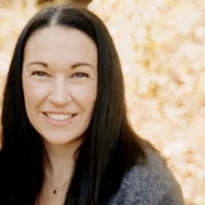 A woman smiling for the camera in front of some leaves.